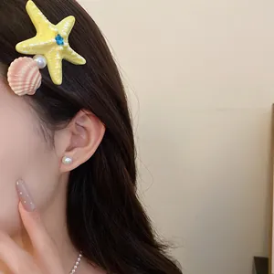 Close-up of vibrant yellow starfish and pink shell hair clip worn on model's side hair for summer