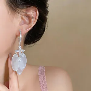 Close-up of silver needle C-shaped hoop earrings with shell tassels and zircons