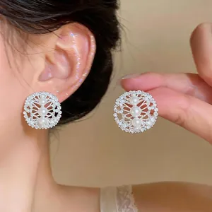 Elegant circular hollowed zircon earrings with central pearls shown on ear and in hand