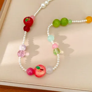 Close-up detail of a colorful resin apple necklace with white pearls for a sweet summer look