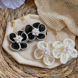 Dettaglio di orecchini a fiore in chiffon con eleganti centri in perla bianchi e neri