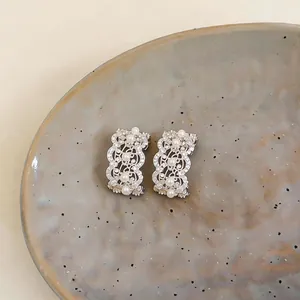 Elegant detail of hollow lace-designed silver earrings with zircons and white pearls