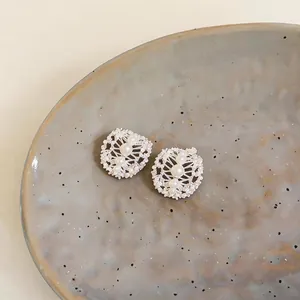 Close-up of hollow oval earrings with zircon and pearls on ceramic plate