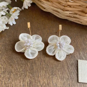 Primo piano di orecchini a fiore in tessuto bianco con dettagli in perle e perni quadrati dorati