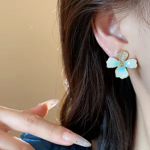 Close-up detail of blue enamel flower earring with 18k gold plating worn on a model's ear