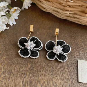 Dettaglio ravvicinato di orecchini eleganti a fiore in chiffon nero con perle e oro
