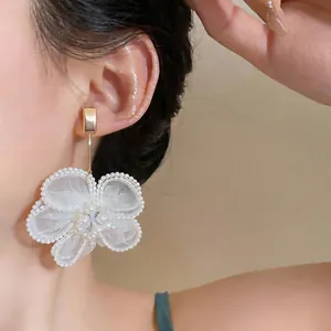 Primo piano di orecchini a fiore in garza bianca con dettagli di perle su una modella