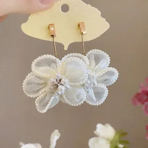 Primo piano di eleganti orecchini a fiore in garza con accenti di perle e ganci dorati