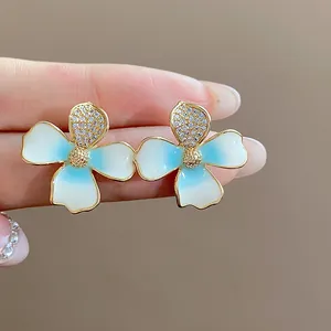 Detailed close-up of 18k gold-plated flower stud earrings with blue enamel and zircons
