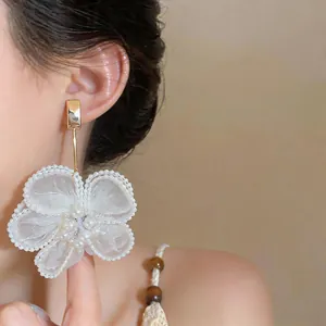 Dettaglio di eleganti orecchini a fiore in chiffon bianco con perle su una modella.
