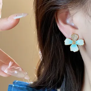 Close-up detail of an 18k gold plated flower stud earring with blue enamel and zircons