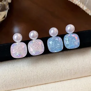 Elegant geometric pearl stud earrings with iridescent square crystals on black display.