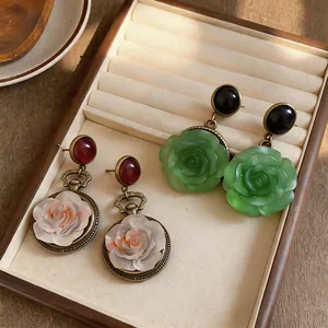 Detailed view of elegant resin rose earrings in white and green on a jewelry tray.