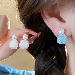 Detailed macro view of elegant geometric pearl stud earrings with iridescent finish on model