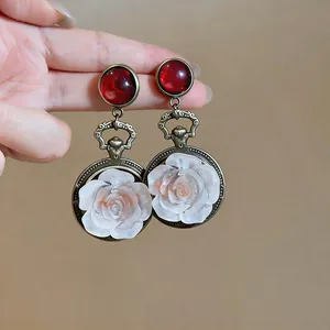 Close-up detail of vintage bronze drop earrings with red cabochons and white resin roses