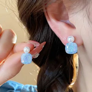 Elegant pearl and blue glitter square stud earrings shown in a close-up on model ear