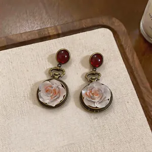 Detailed view of vintage style resin white rose earrings with red cabochon on beige fabric