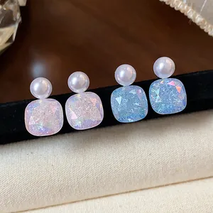 Close-up of geometric pearl stud earrings with iridescent blue and purple crystals