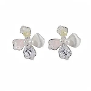 Eleganti orecchini a fiore con perle e zirconi colorati su sfondo bianco lucido.