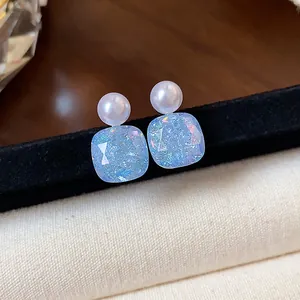 Detail view of geometric pearl stud earrings with iridescent blue square drops