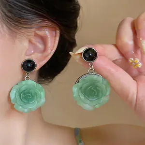 Close-up of light green resin rose drop earrings worn on ear, showing delicate floral detail.