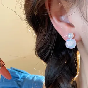 Detail view of iridescent geometric stud earrings with pearl accent on model ear