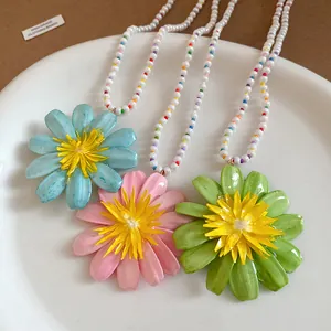 Macro view of three resort-style beaded necklaces with large flower pendants in vibrant colors.