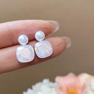 Detail shot of pearl stud earrings with iridescent square glitter stone charms.