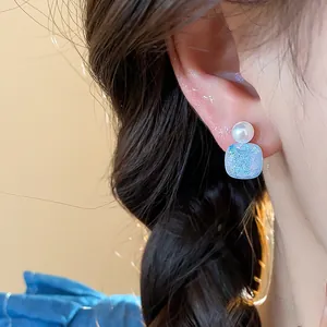 Detail shot of geometric pearl stud earrings with blue iridescent glitter texture