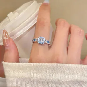 Dettaglio di un elegante anello aperto con zircone blu quadrato indossato al dito, stile