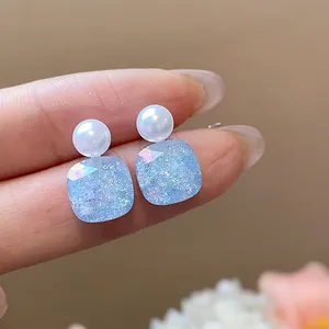 Elegant detail of geometric pearl stud earrings featuring a shimmering blue square