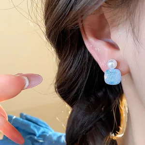 Macro view of minimalist square blue glitter earrings with white pearl detail