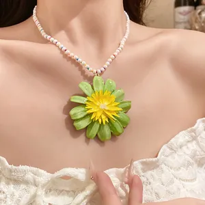 Close-up of a vibrant green and yellow flower pendant on a beaded pearl necklace.