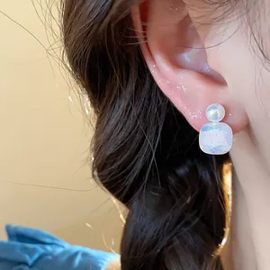 Close-up of elegant pearl and iridescent geometric stud earring on ear