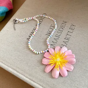 Top-down view of a pearl beaded necklace with a large pink flower pendant on a book.