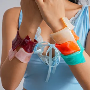 Detailed view of colorful irregular resin bangles worn on both wrists by a model
