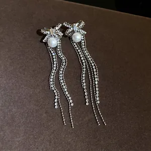 Detailed view of silver bow earrings with elegant pearl and long sparkling rhinestone tassels