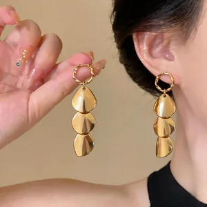 Close-up detail of elegant gold triple-drop metallic earrings worn by a model