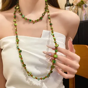 Detail view of a Bohemian style long necklace with green shell beads worn by a model