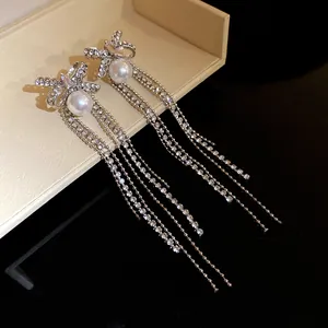 Close-up of elegant rhinestone pearl bow knot earrings with long tassels.