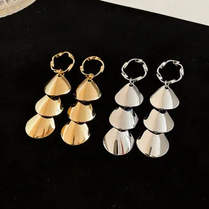 Close-up of tiered metallic drop earrings in gold and silver finish on black background.