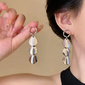 Close-up of silver minimalist earrings with three glossy metallic droplets on an ear.