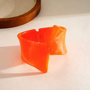 Detail shot of a bright orange resin bangle with a unique twisted geometric design