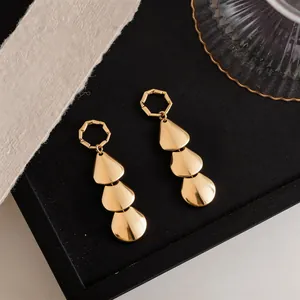 Detail view of gold tiered teardrop earrings with a smooth polished finish on a black tray.