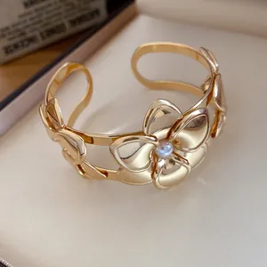 Detailaufnahme eines eleganten goldenen Blumenarmreifs mit einer zentralen Perlenverzierung.