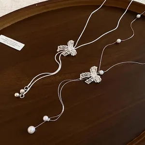 Elegant Y-shaped long necklace with crystal bows and white pearls on wooden tray