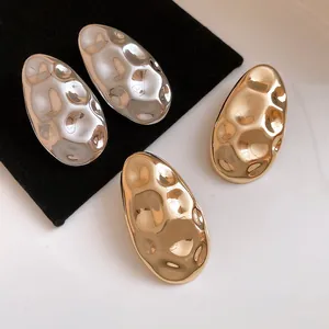 Close-up detail of vintage style hammered oval metallic stud earrings in gold and silver