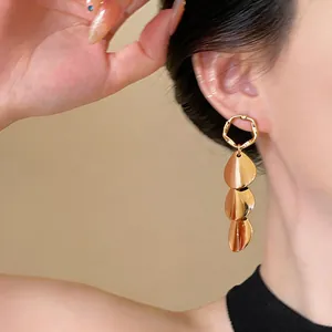 Close-up detail showing a model wearing minimalist golden tiered metallic leaf drop earrings