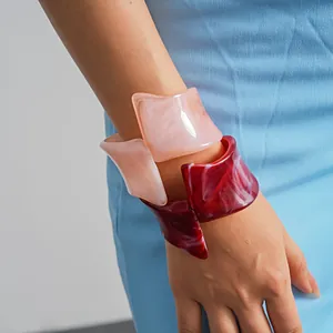 Close-up of irregular marbled resin bangles in pink and red on a model's wrist