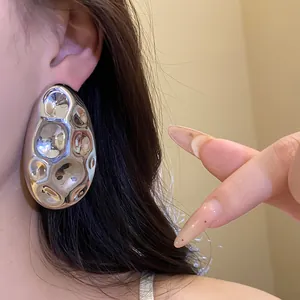 Detailed close-up showing a large irregular silver oval hammered metallic stud earring on ear.